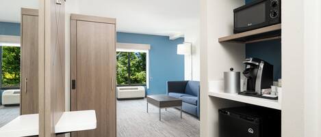 A modern hotel room with a wooden wardrobe, a blue sofa, a coffee machine, and a microwave on a shelf.