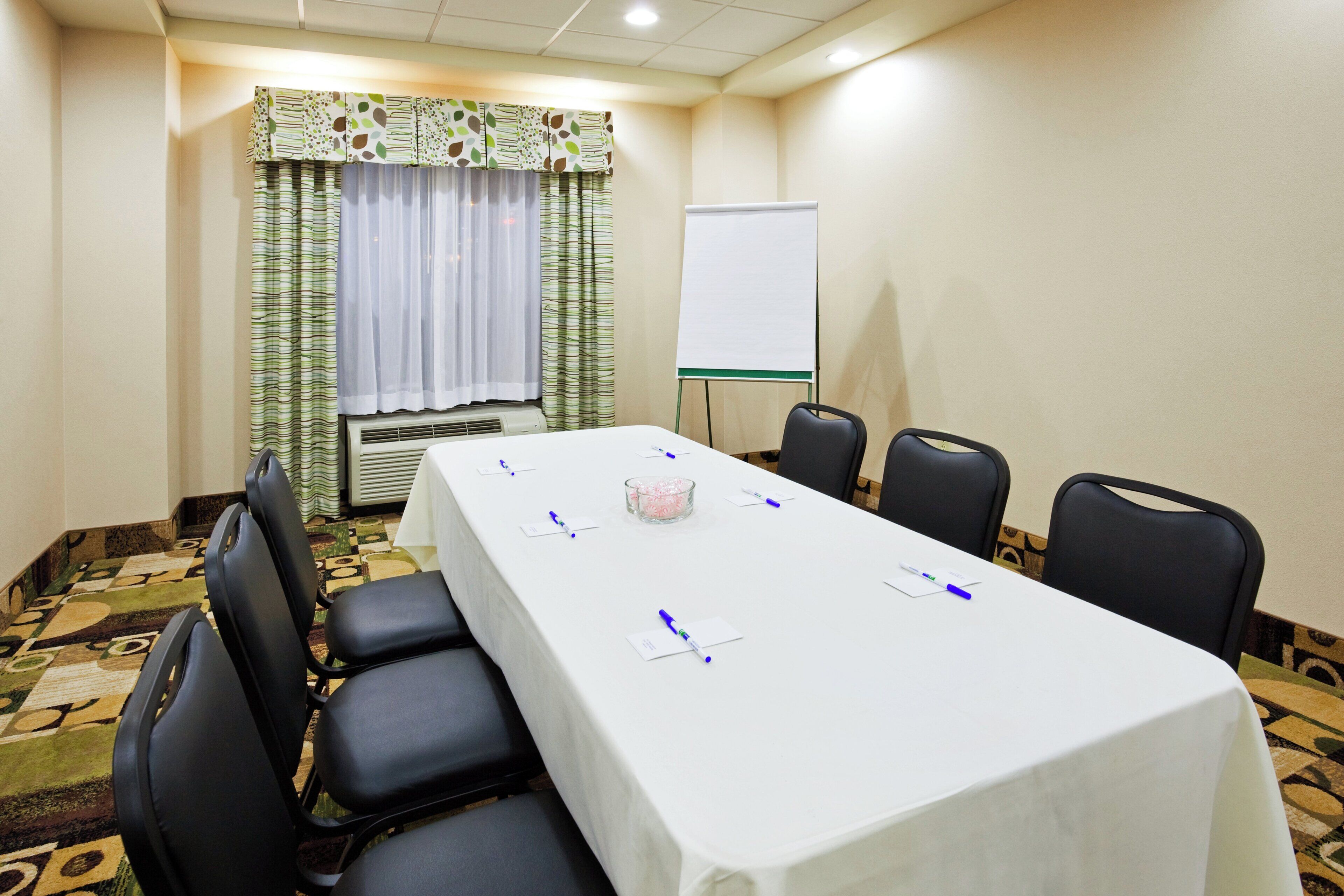 Una sala de conferencias con una larga mesa, sillas, una pizarra y una cortina estampada.