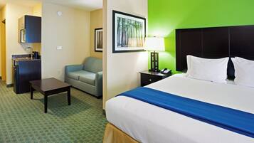 A hotel room with a bed, a desk, a chair, a sofa, a nightstand, a lamp, and a framed picture on the wall.