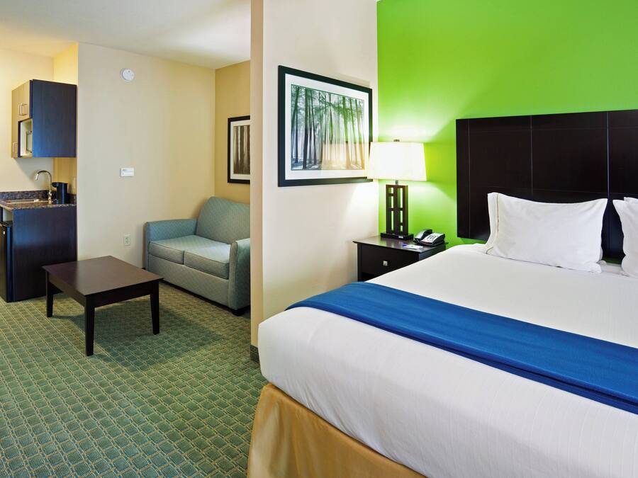 A hotel room with a bed, a desk, a chair, a sofa, a nightstand, a lamp, and a framed picture on the wall.
