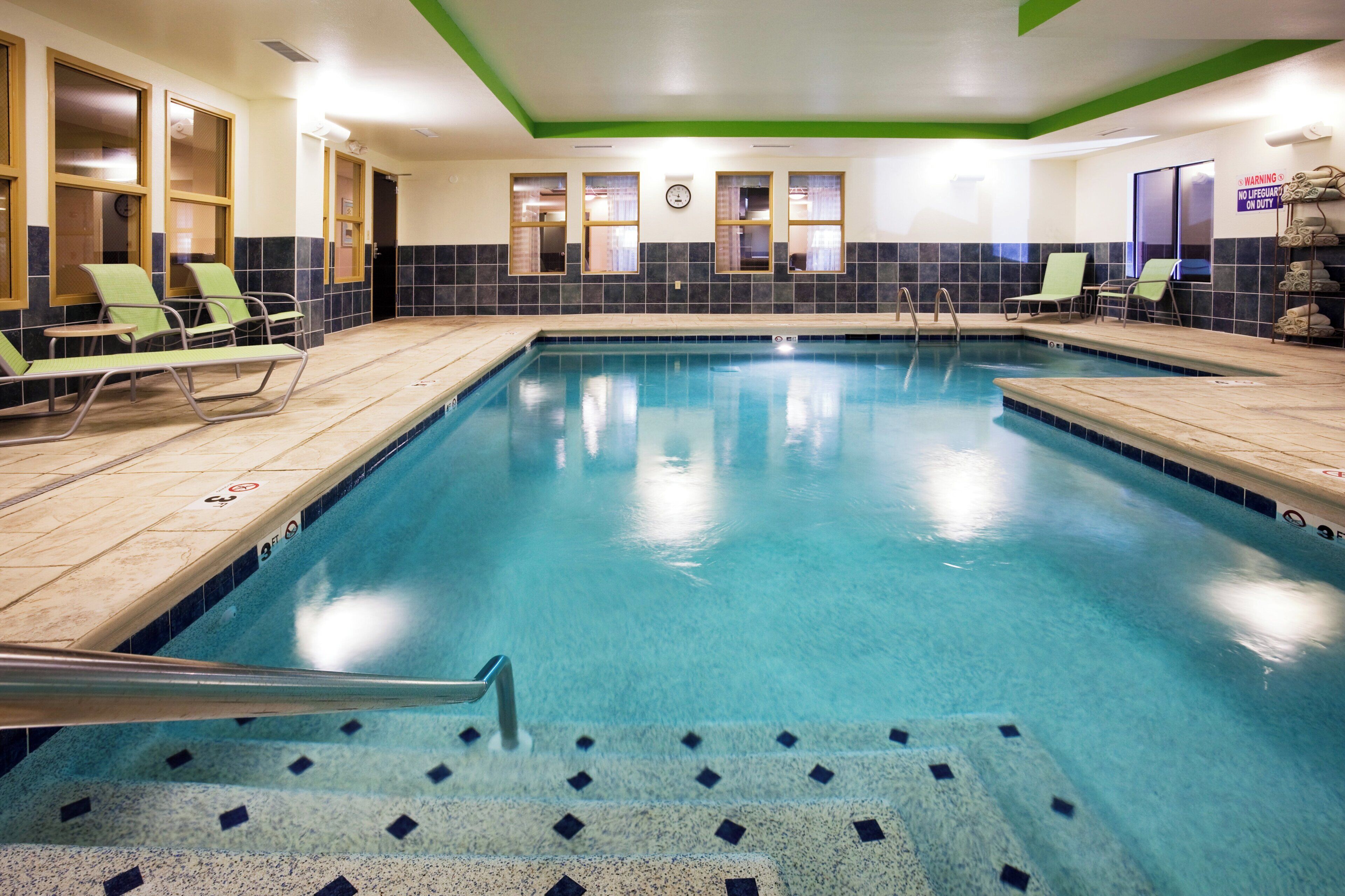 Una piscina interior con agua cristalina, rodeada de sillas de descanso y un muro de azulejos.