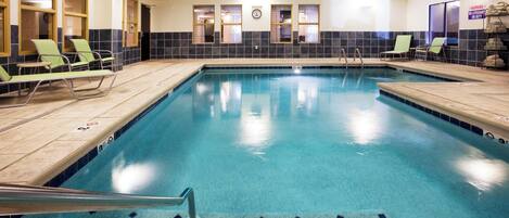 Una piscina interior con agua cristalina, rodeada de sillas de descanso y un muro de azulejos.