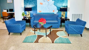 A lobby with a blue sofa set, two side tables with lamps, a coffee table, and a large wall map.
