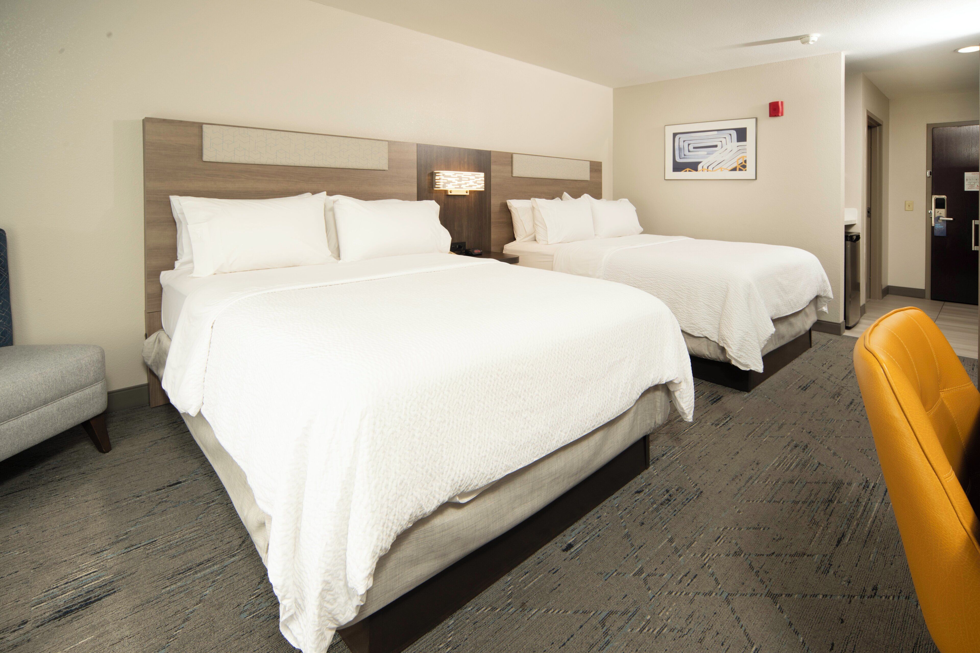A hotel room with two beds, a small seating area, and a door leading to the bathroom.