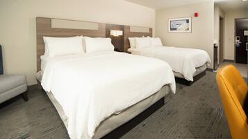 A hotel room with two beds, a small seating area, and a door leading to the bathroom.