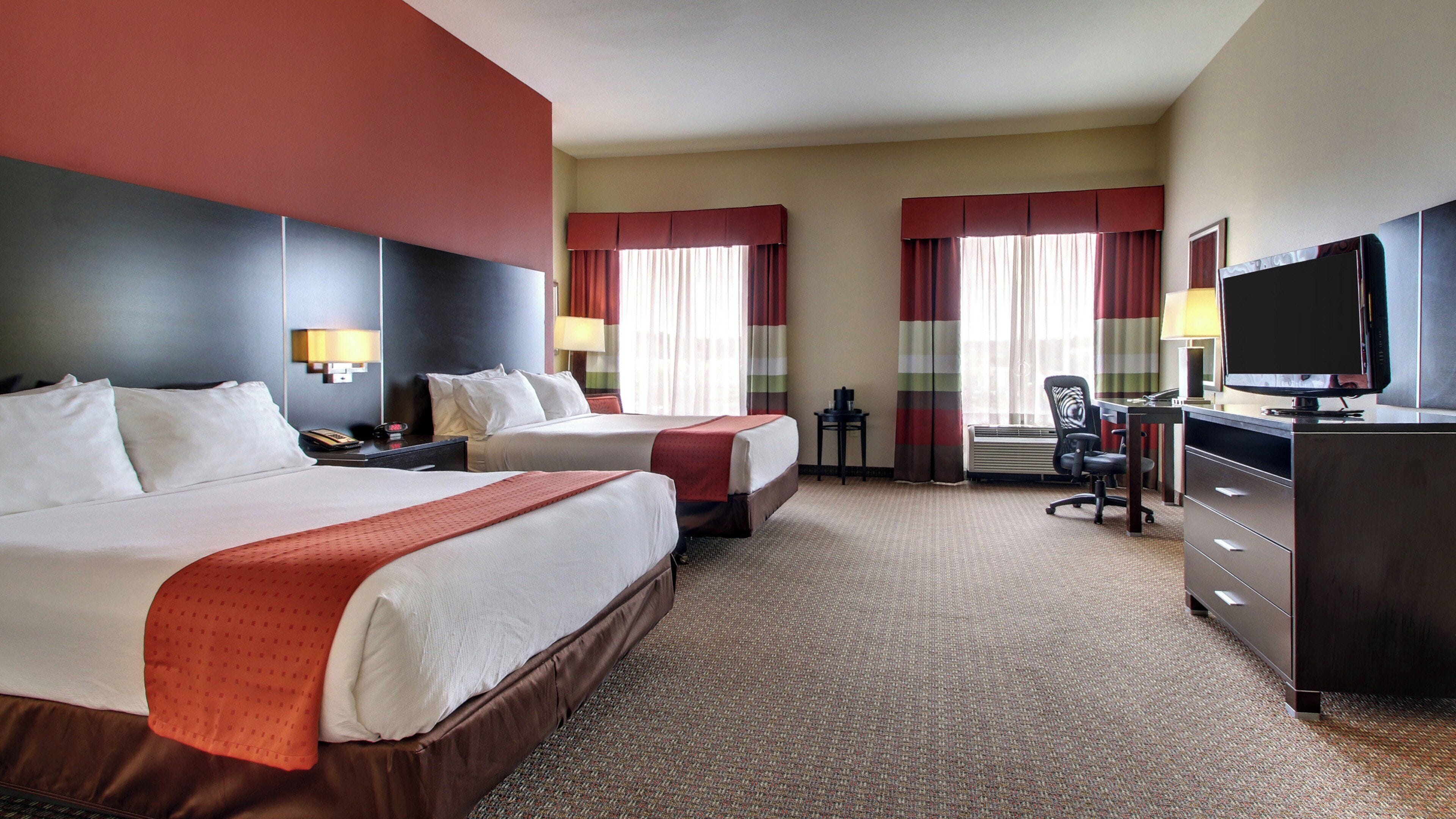 A hotel room with two beds, a desk with a television, and a chair.