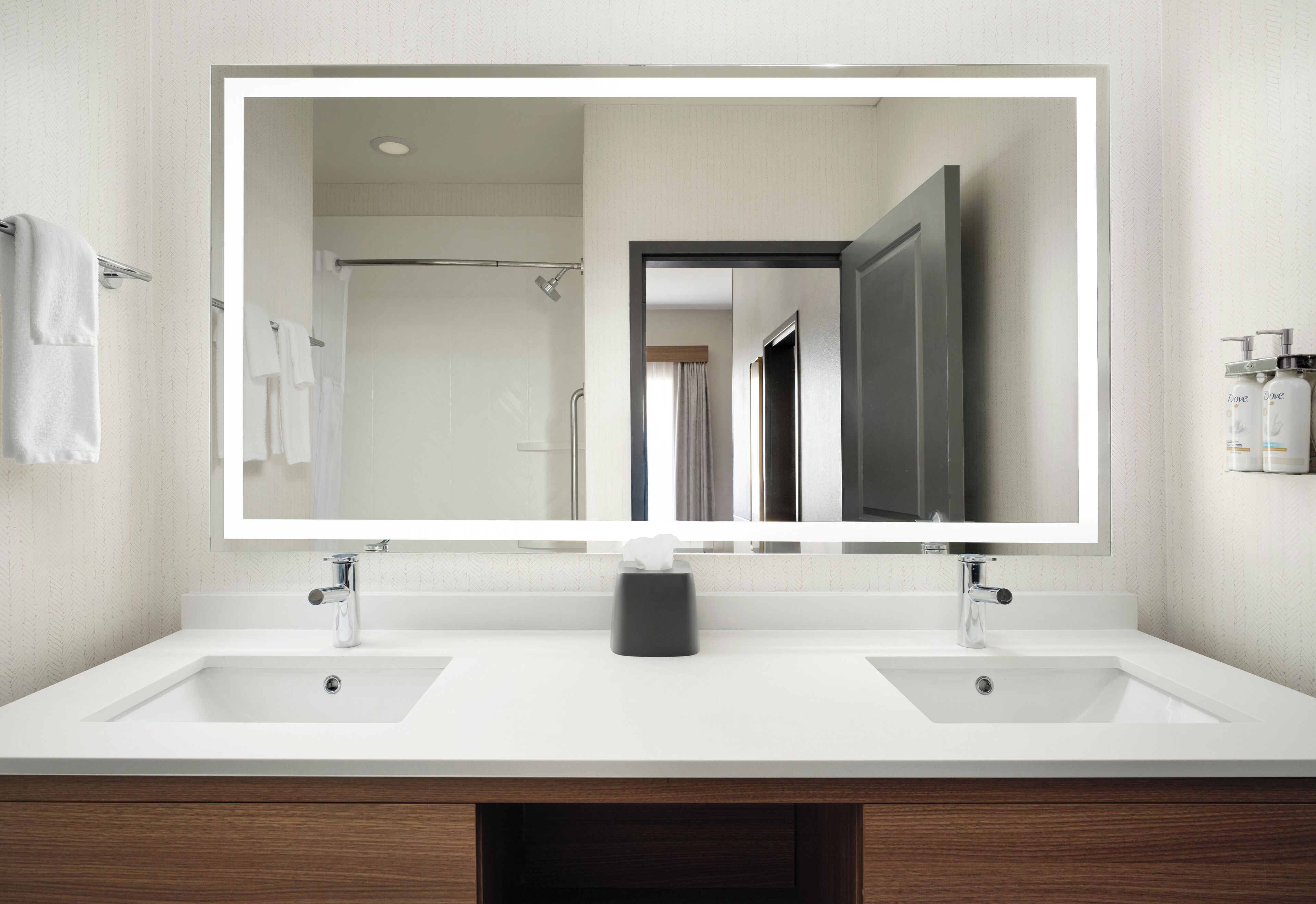 A bathroom with a large mirror, two sinks, and a towel rack.
