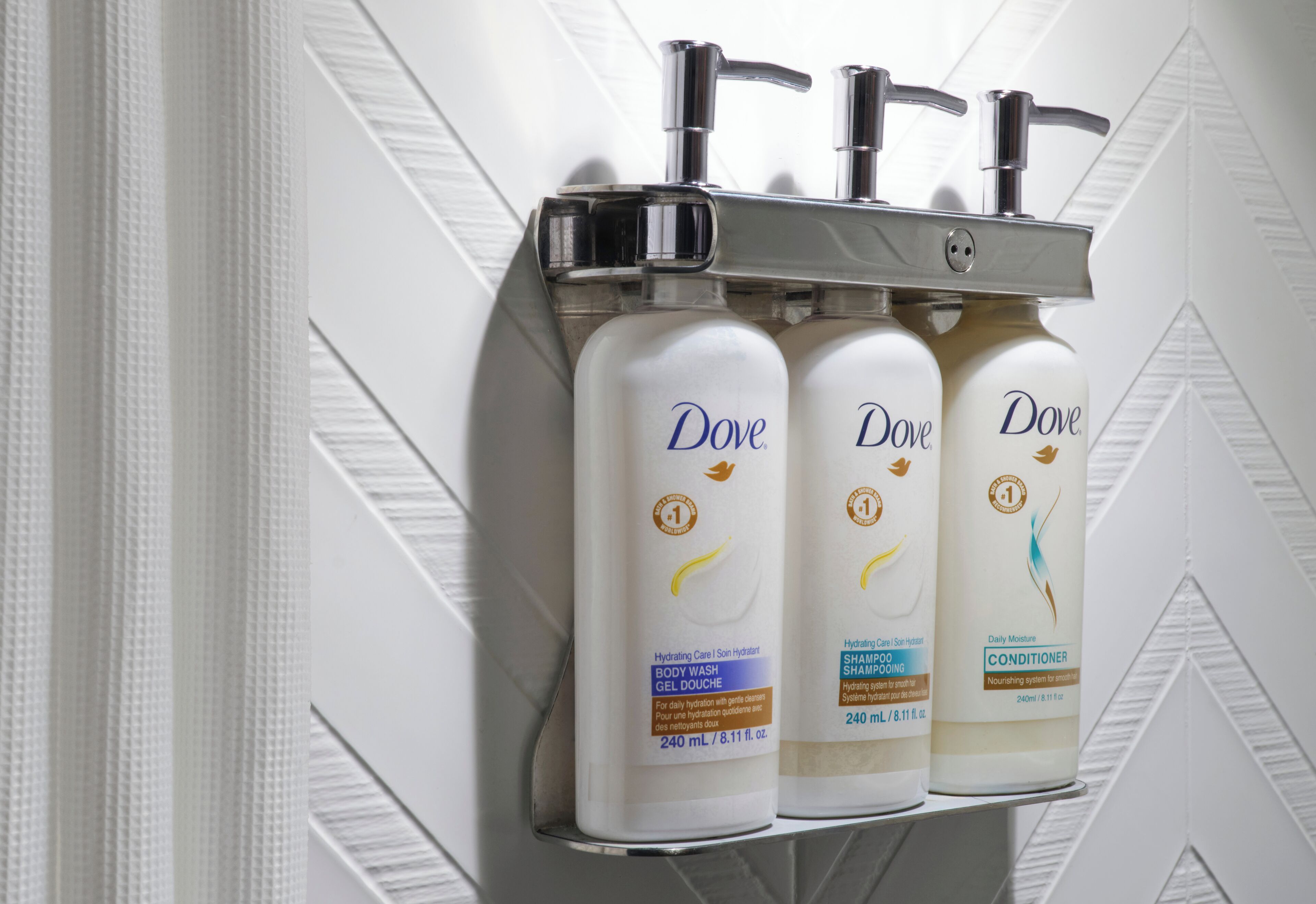 Three Dove body wash, shampoo, and conditioner bottles mounted on a wall.