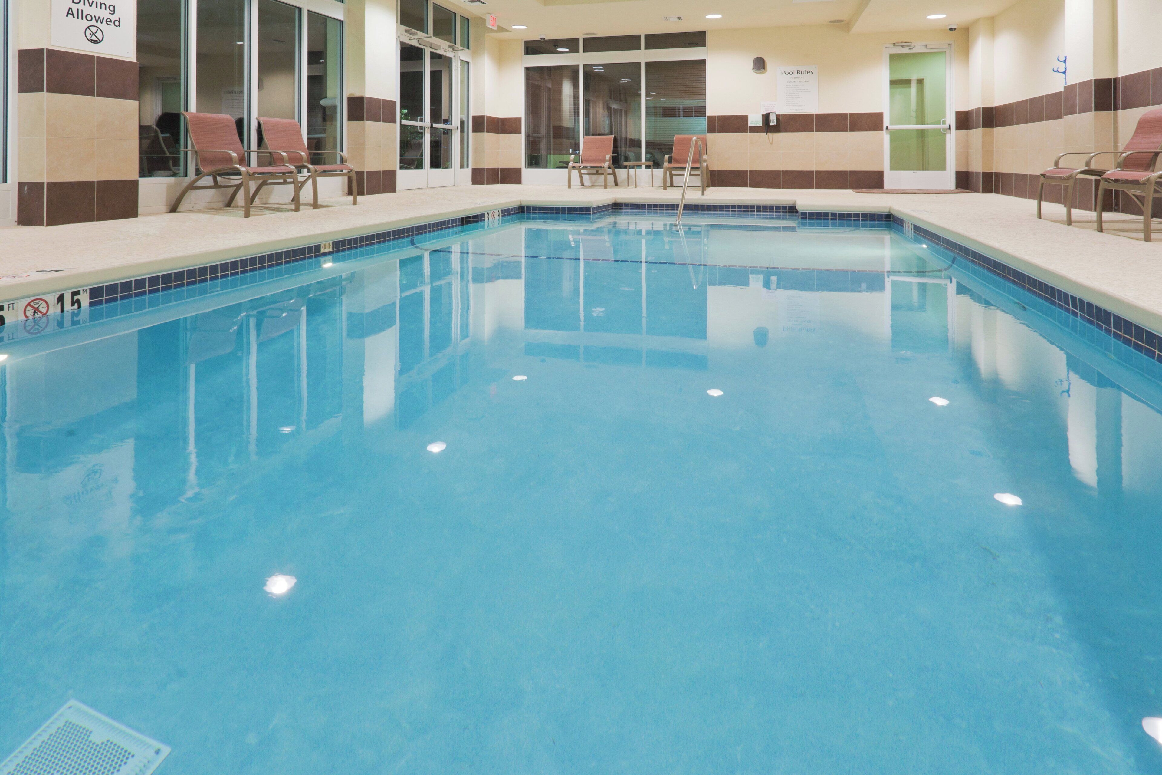 A clear indoor swimming pool with a tiled edge, lounge chairs, and a sign indicating diving is allowed.
