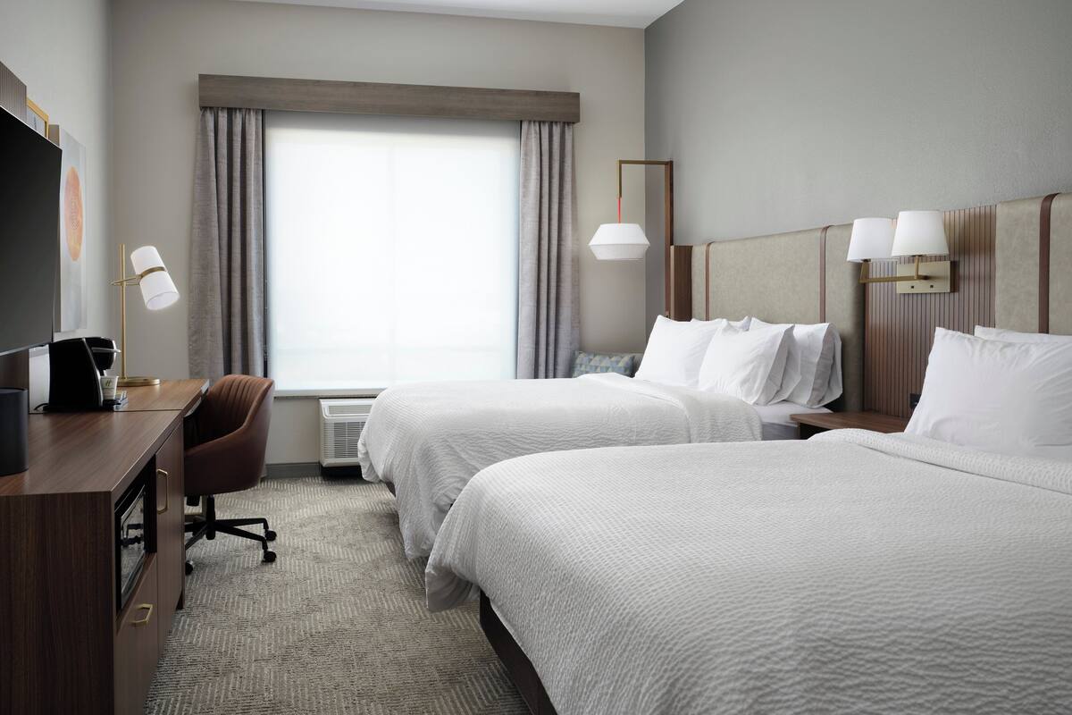 A hotel room with two beds, a desk, a chair, and a TV.