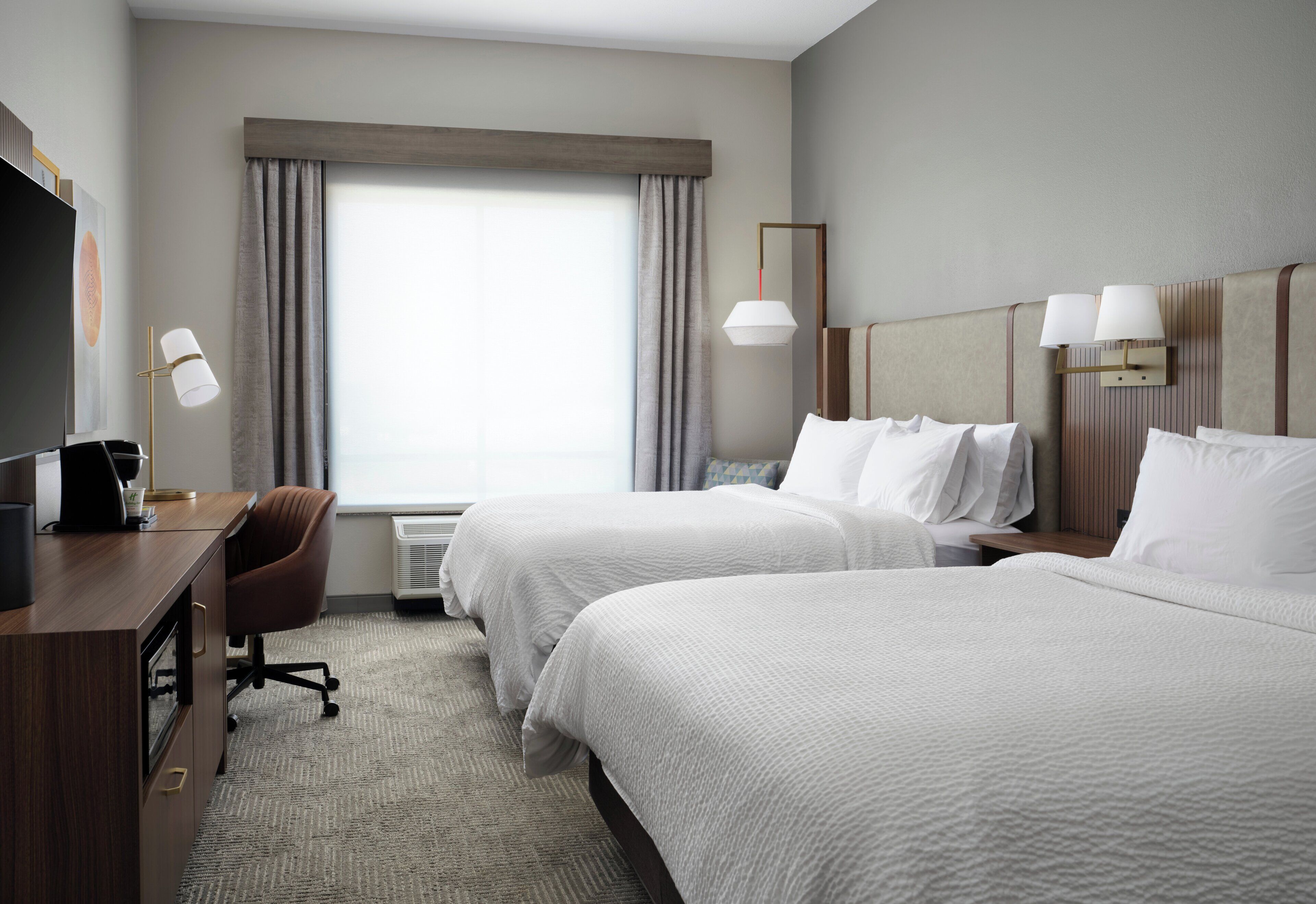 Habitación de hotel con dos camas, un escritorio, una silla y un televisor.