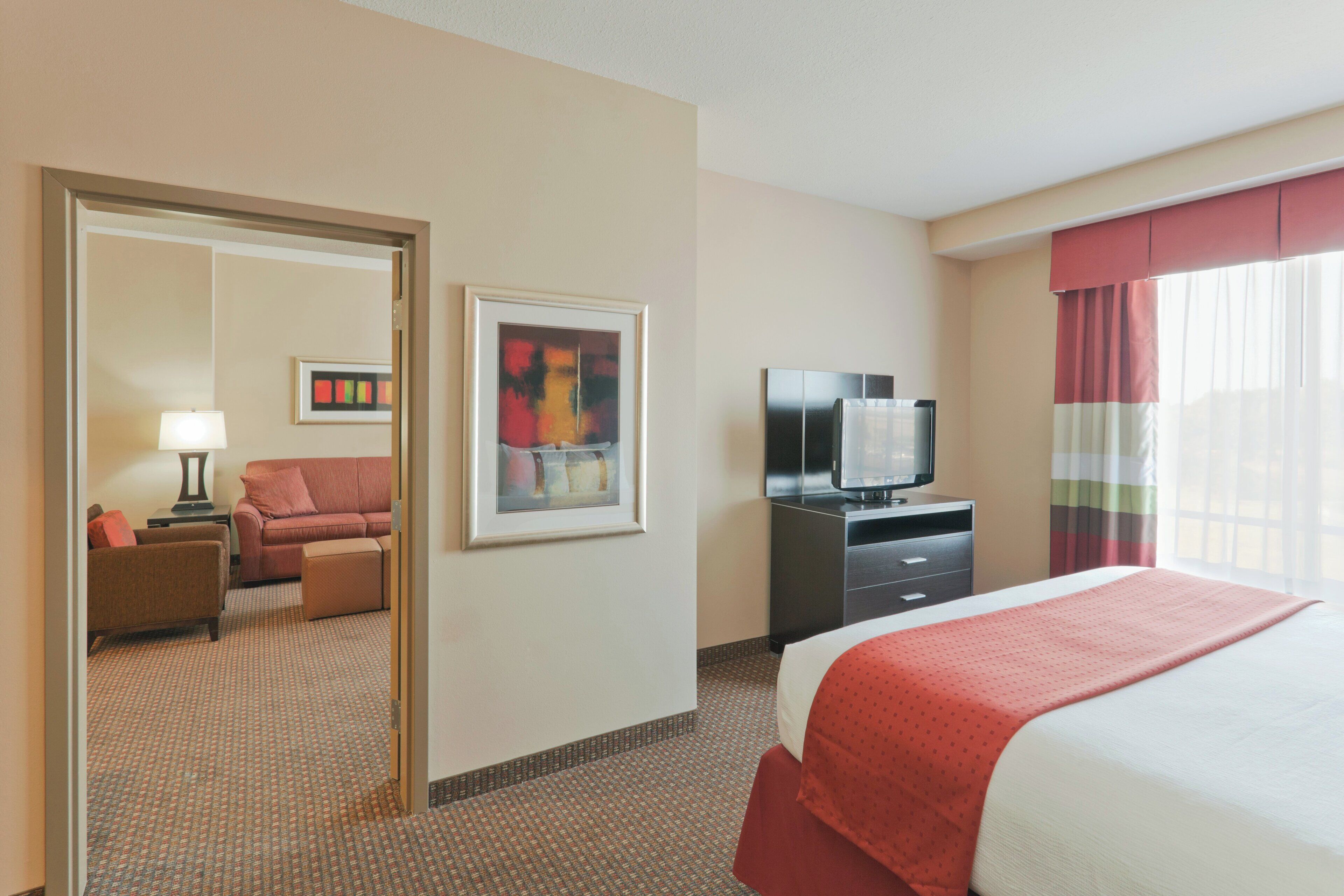 A hotel room with a bed, a television, a desk, a chair, a sofa, and a painting on the wall.