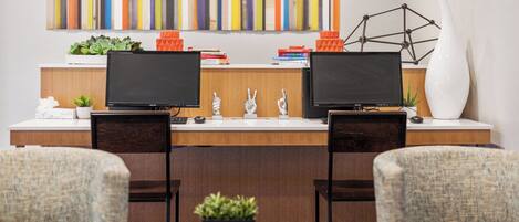 A modern office space with two monitors, a desk, two chairs, a small table with a plant, and a colorful abstract painting on the wall.