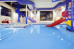 Una piscina interior con piso azul, un tobogán rojo y una escalera azul.