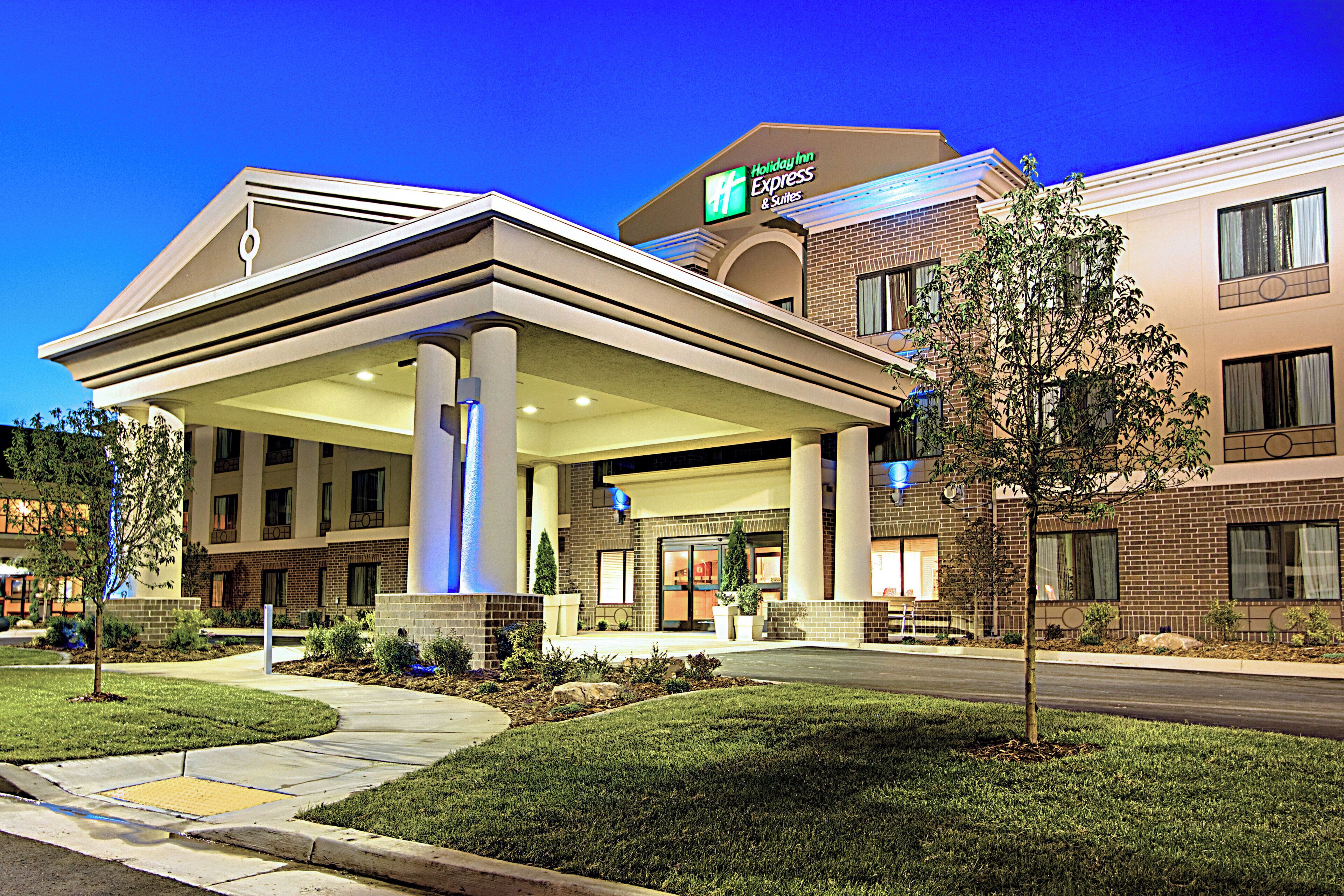 A Holiday Inn Express & Suites hotel with a covered outdoor area, brick facade, and landscaped surroundings.