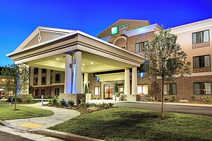 Un hotel Holiday Inn Express & Suites con un espacio exterior cubierto, fachada de ladrillo y jardines.