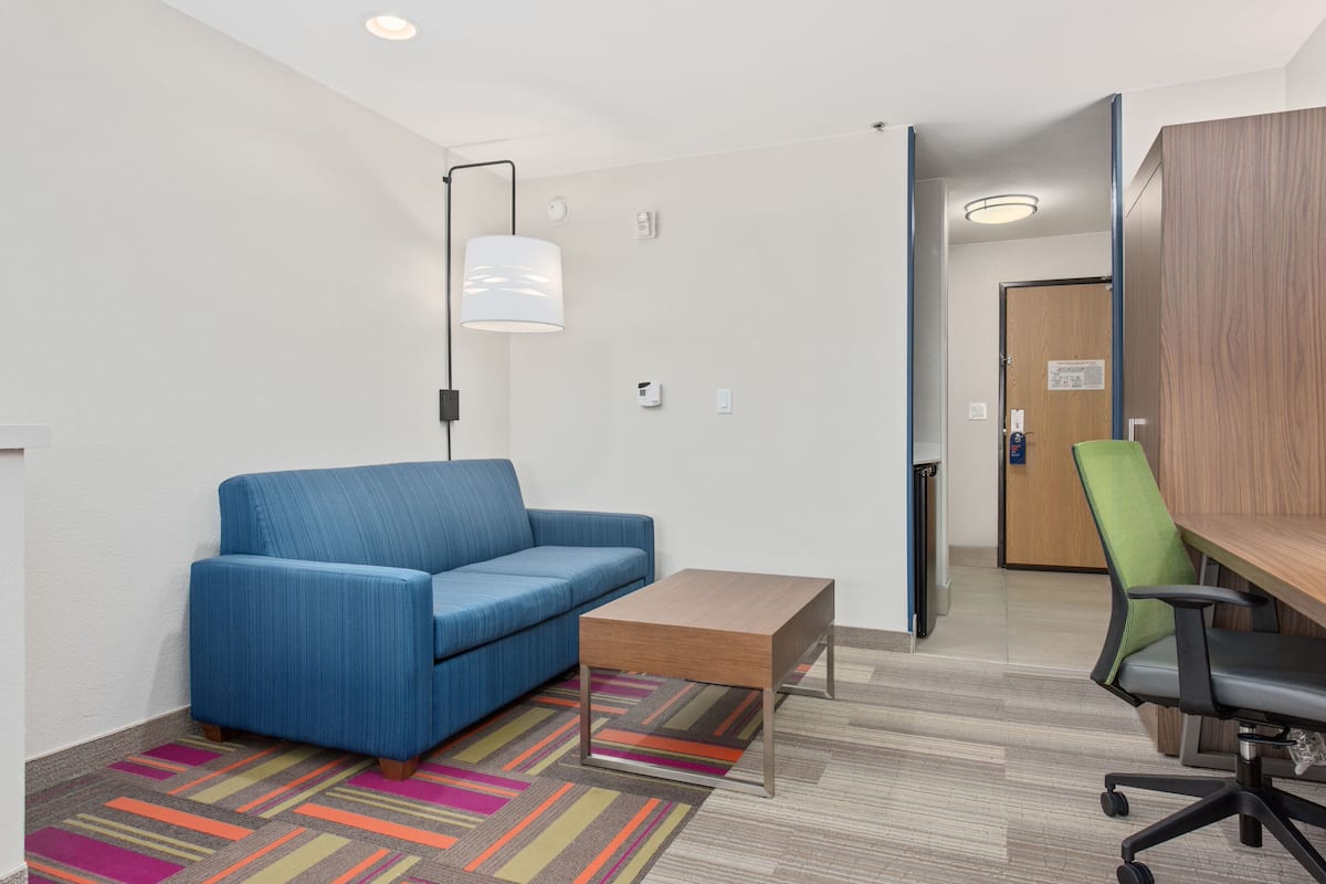 Un espace de bureau moderne avec un canapé bleu, une table basse en bois, un fauteuil de bureau vert et un bureau avec une lampe.