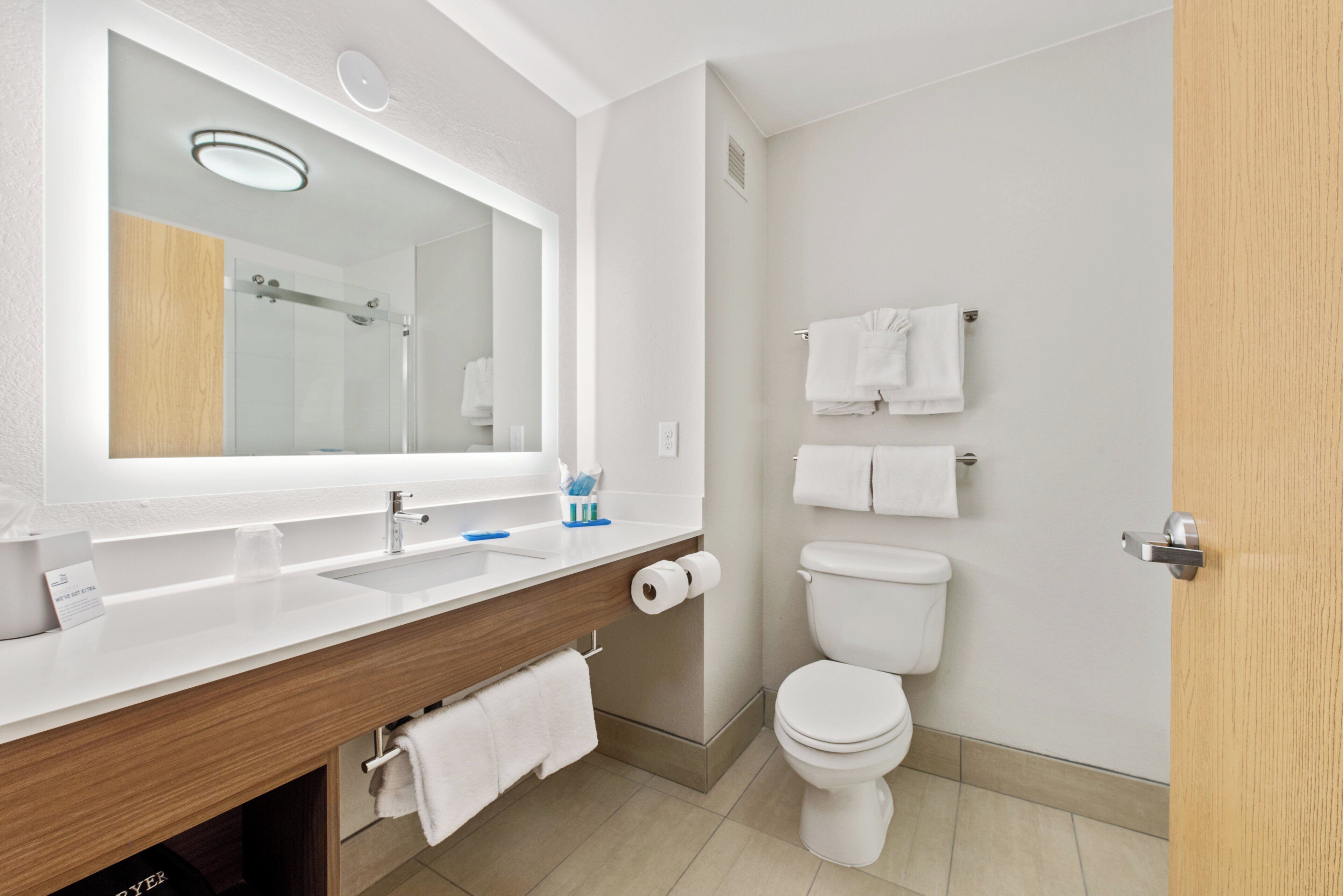 A modern bathroom with a large mirror, a wooden vanity, a toilet, and a shower area.