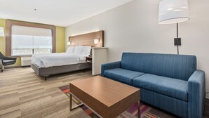 A hotel room with a bed, a blue sofa, a wooden coffee table, and a large window.