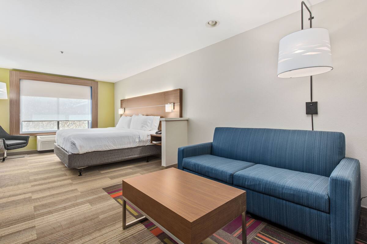 Une chambre d’hôtel avec un lit, un canapé bleu, une table basse en bois et une grande fenêtre.