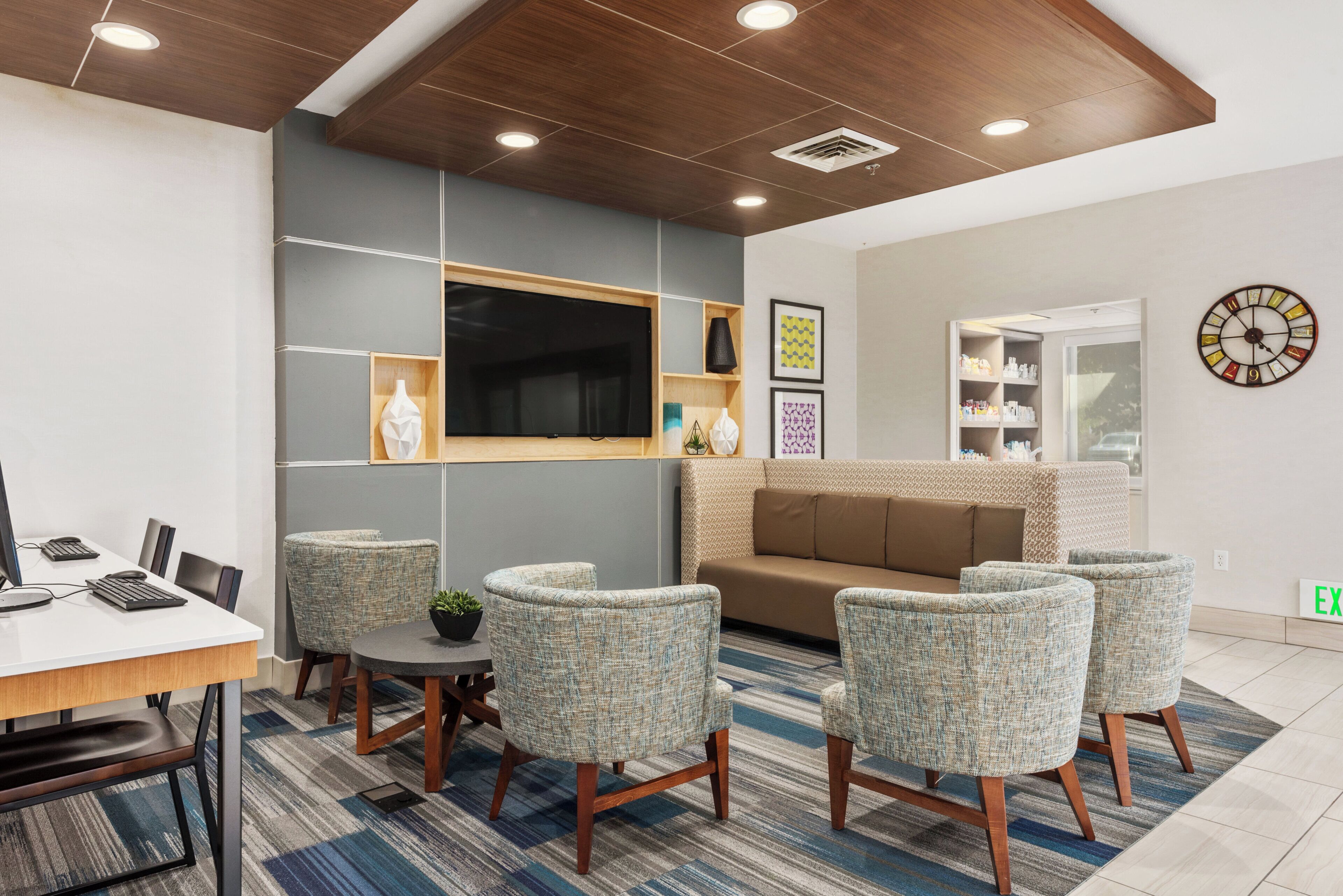 A modern waiting area with a reception desk, seating, a television, and a clock on the wall.