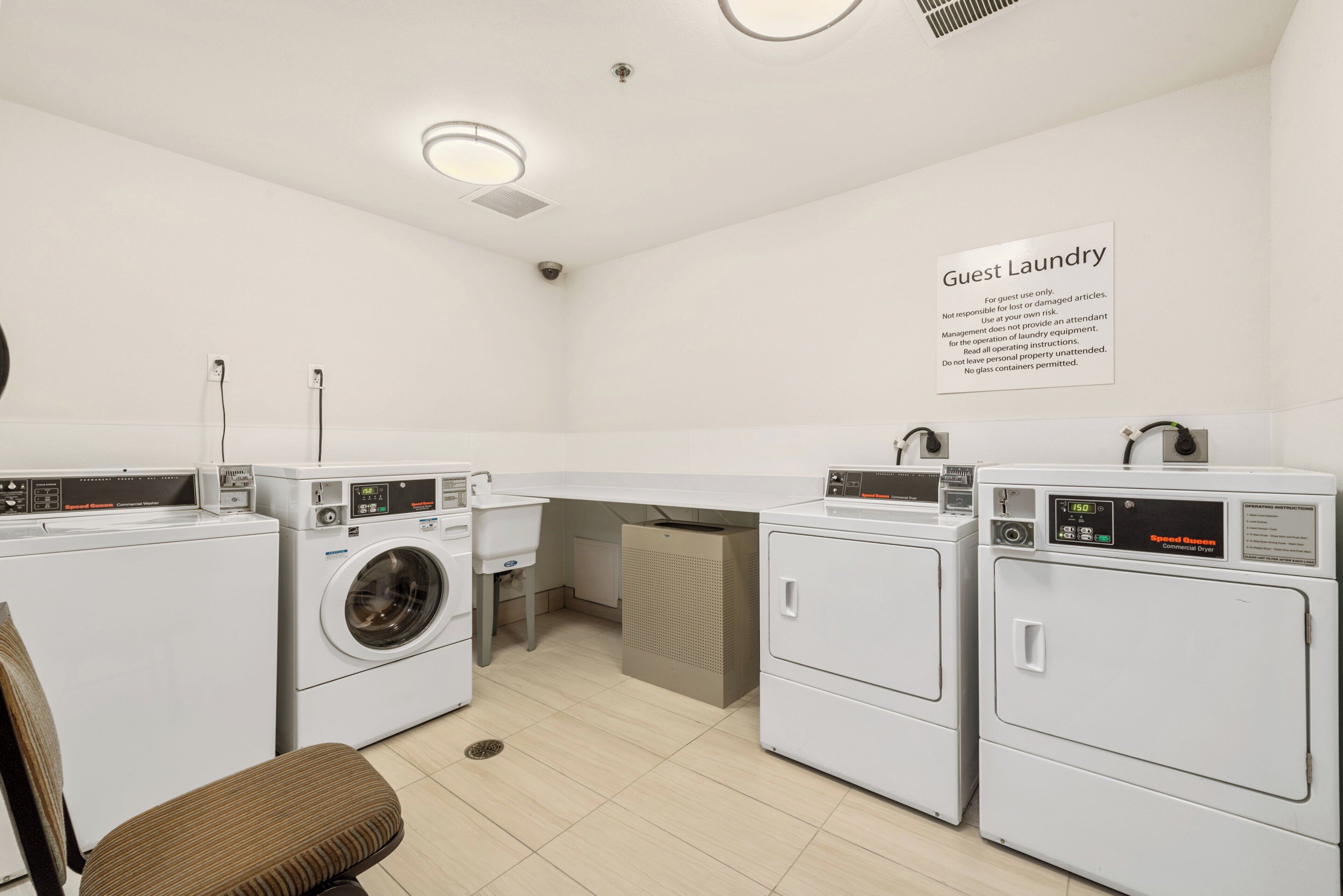 A guest laundry area with multiple washing machines, a sink, and a chair.
