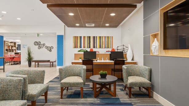A modern reception area with a wooden ceiling, two desks with computers, comfortable seating, and a colorful abstract painting on the wall.