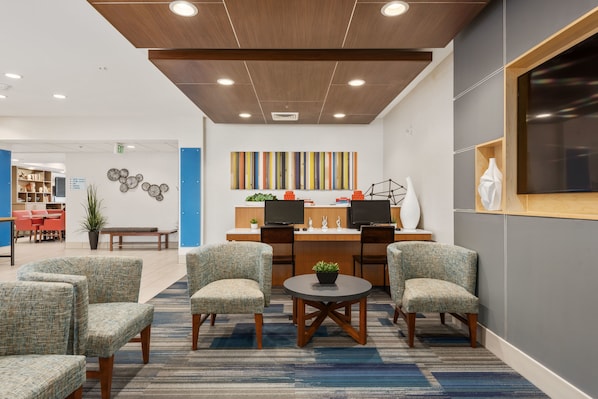 A modern reception area with a wooden ceiling, two desks with computers, comfortable seating, and a colorful abstract painting on the wall.