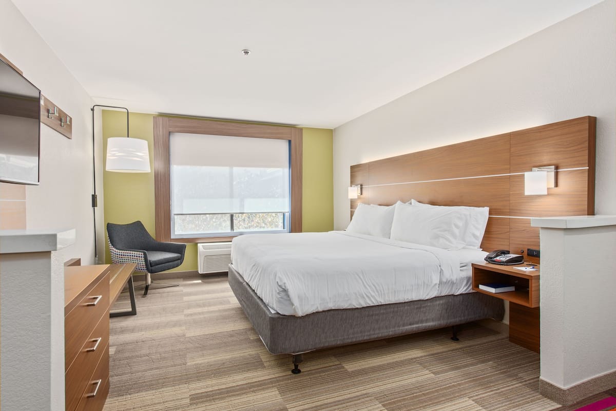 Une chambre d’hôtel moderne avec un grand lit, une table de chevet, une lampe et une chaise.