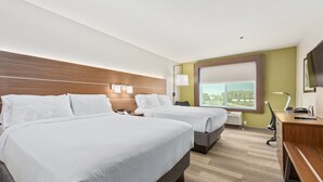 A hotel room with two beds, a desk, a chair, and a large window offering a city view.