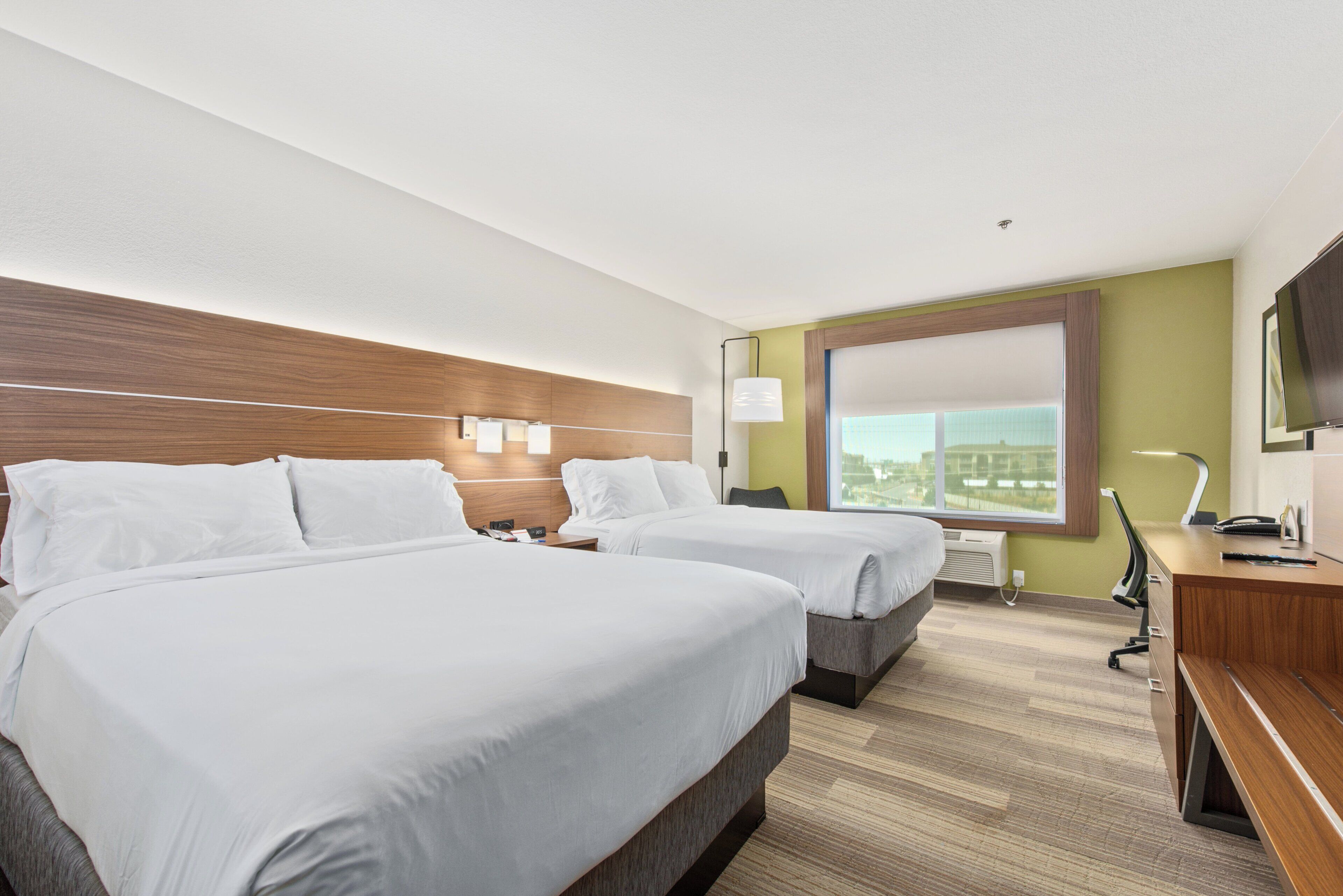 A hotel room with two beds, a desk, a chair, a TV, and a window with a view.