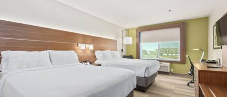 A hotel room with two beds, a desk, a chair, a TV, and a window with a view.