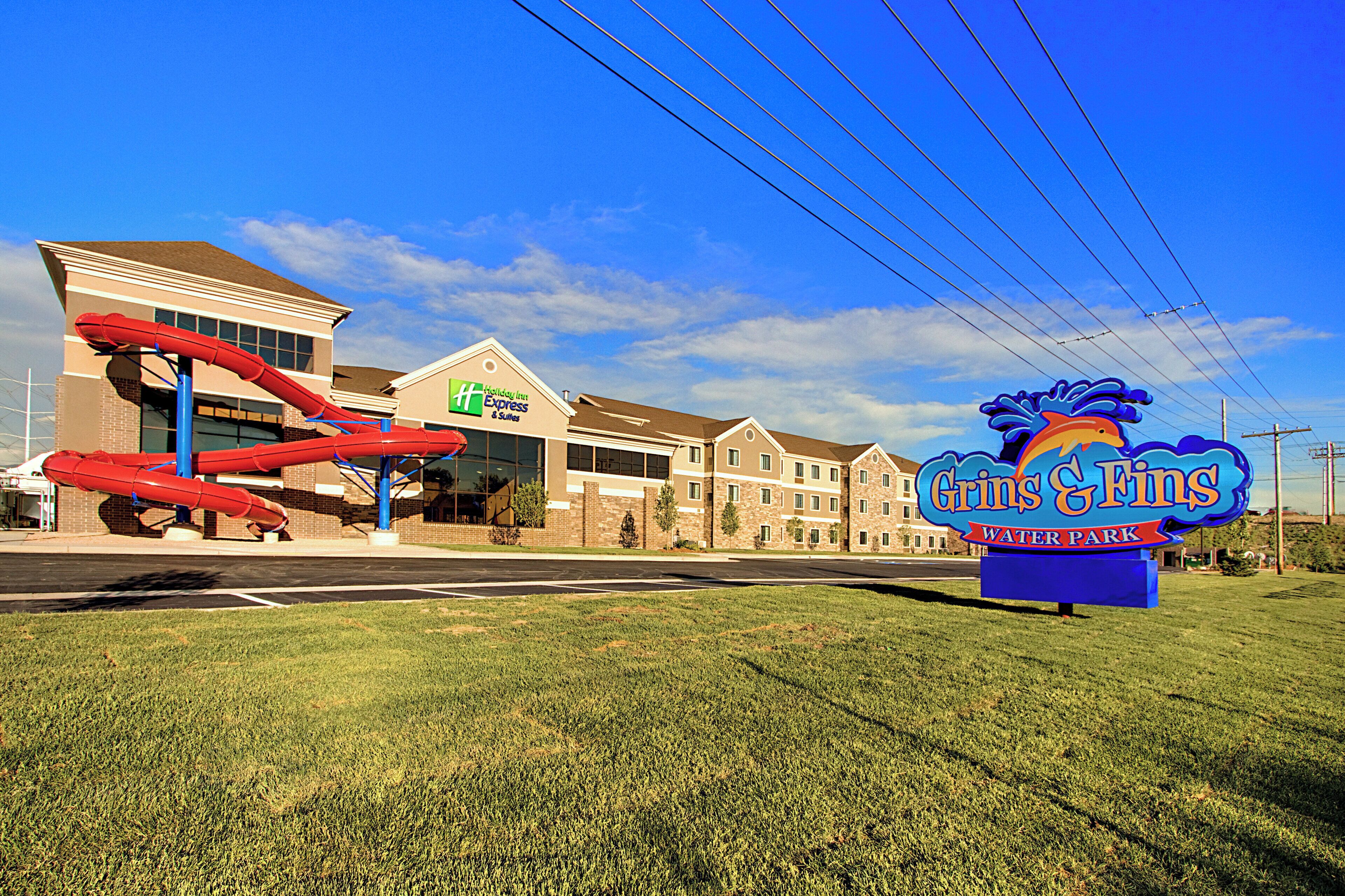 Un hôtel avec une grande enseigne indiquant le parc aquatique Grins & Grins, un bâtiment Holiday Inn Express & Suites, et une structure de toboggan aquatique rouge.