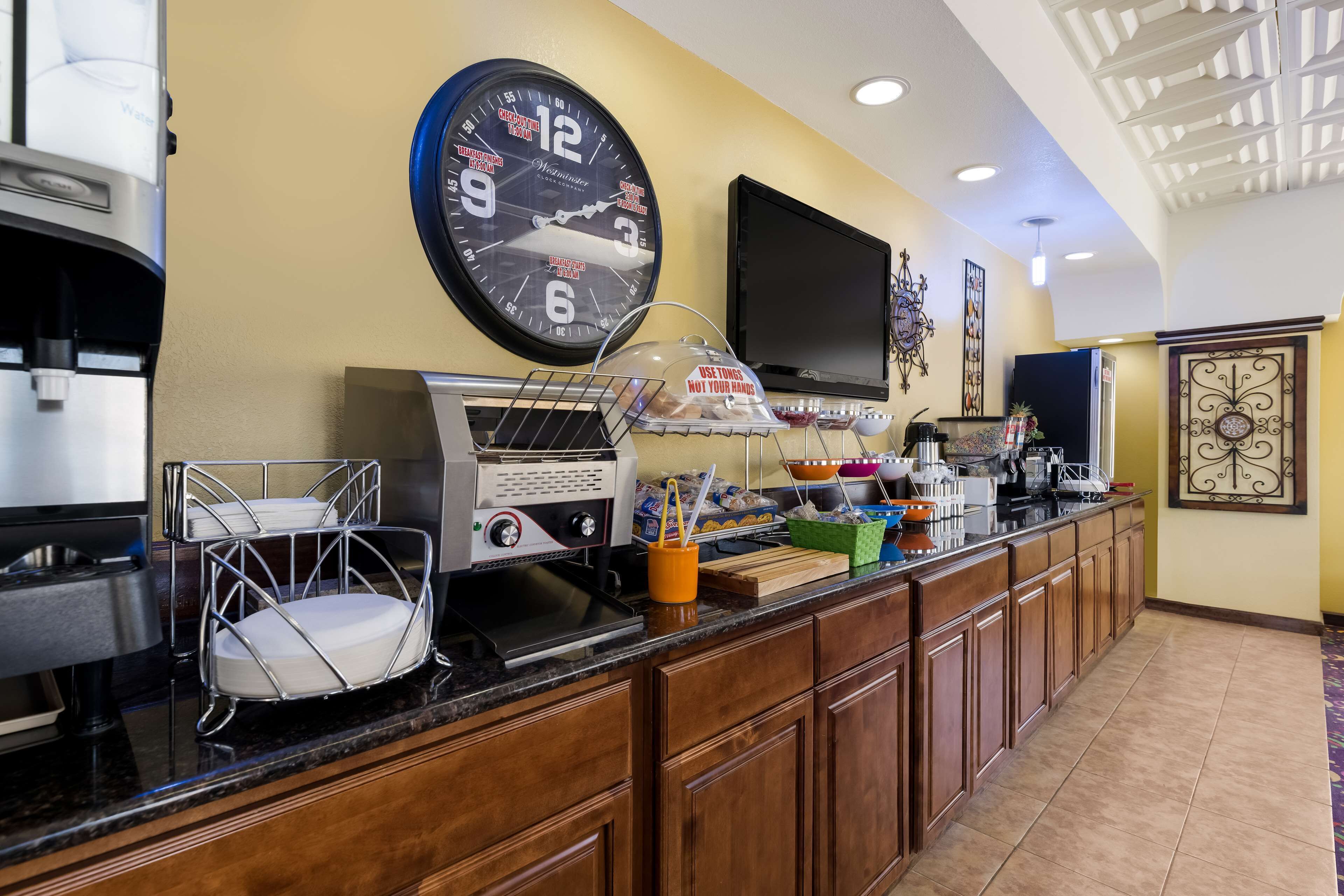 Un hall de hotel con una estación de café, un reloj, un televisor y un adorno en la pared.