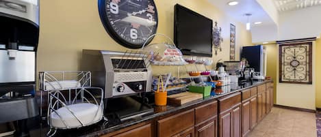 Un hall de hotel con una estación de café, un reloj, un televisor y un adorno en la pared.