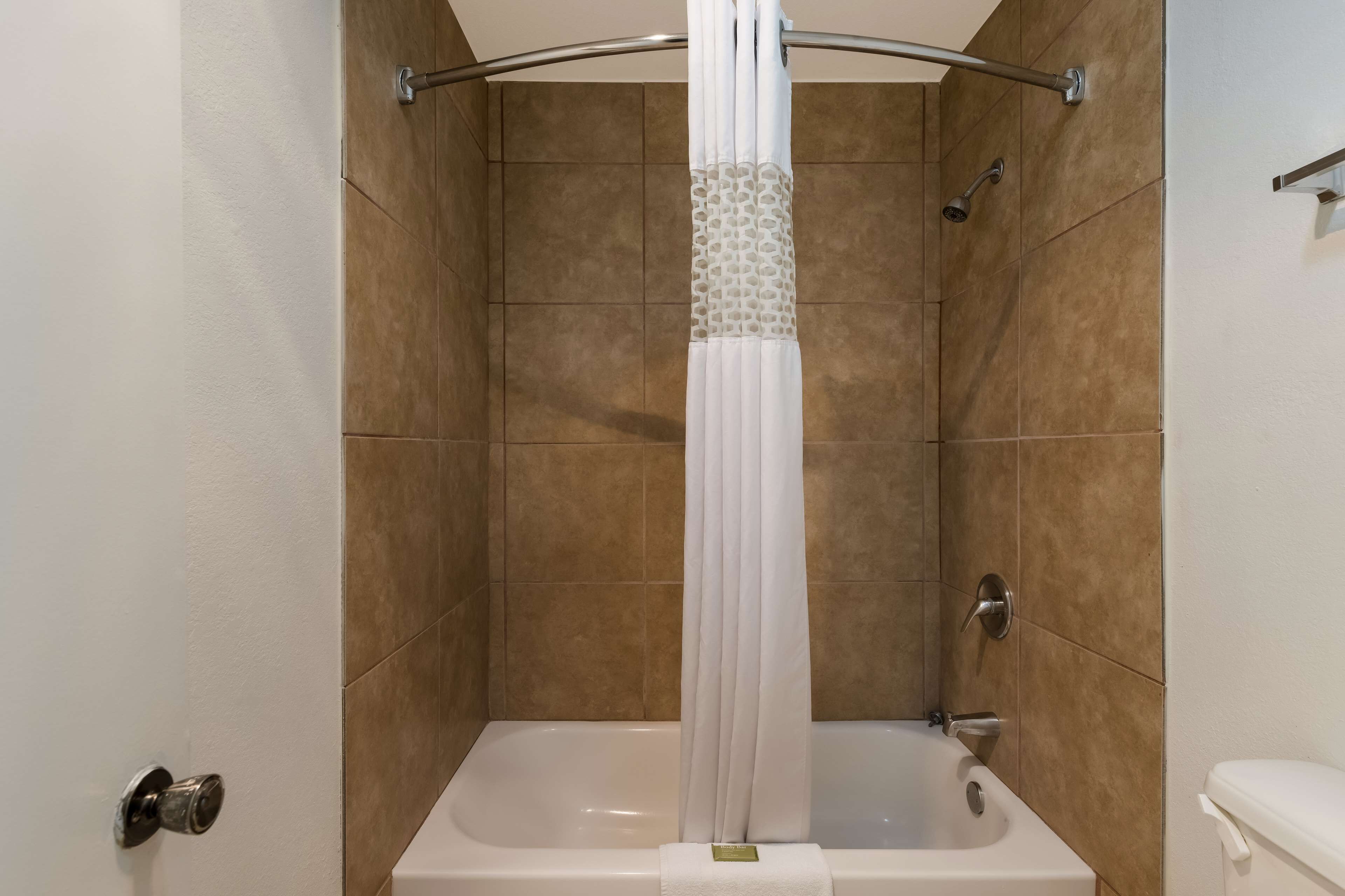A shower with a white curtain, a bathtub, and a showerhead.