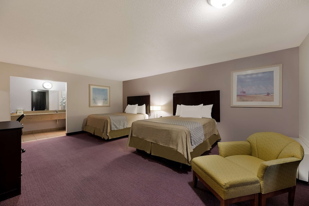 A hotel room with two beds, a chair, a desk, and a mirror.