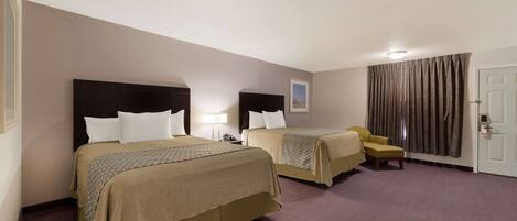 A hotel room with two beds, a chair, a desk, a lamp, and a door.