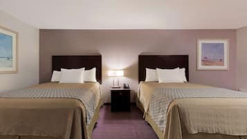 A hotel room with two beds, a nightstand with a lamp, and framed pictures on the walls.