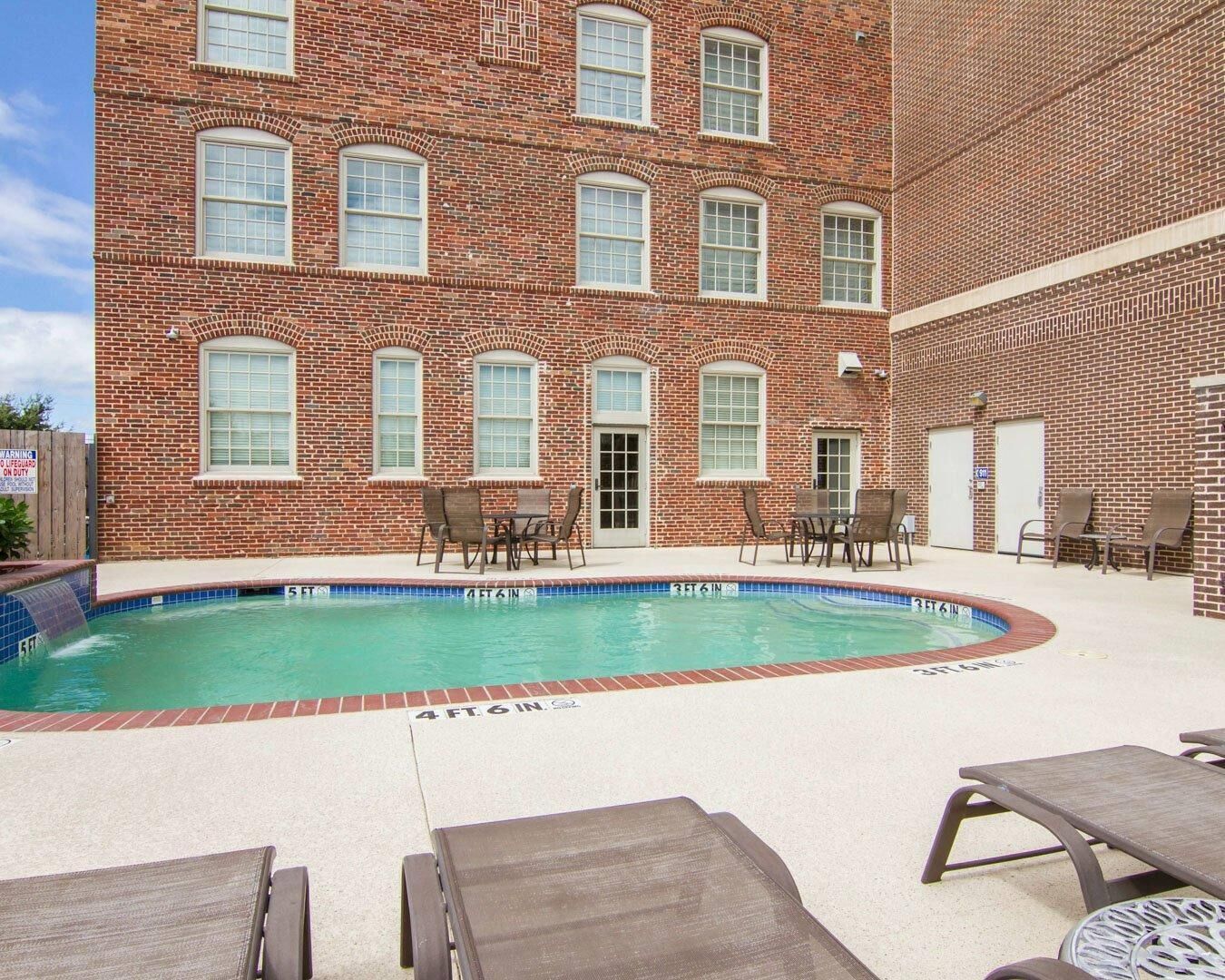 A brick building with a swimming pool, outdoor seating, and a lifeguard warning sign.