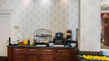 A buffet setup with a coffee maker, a microwave, and a fruit display.