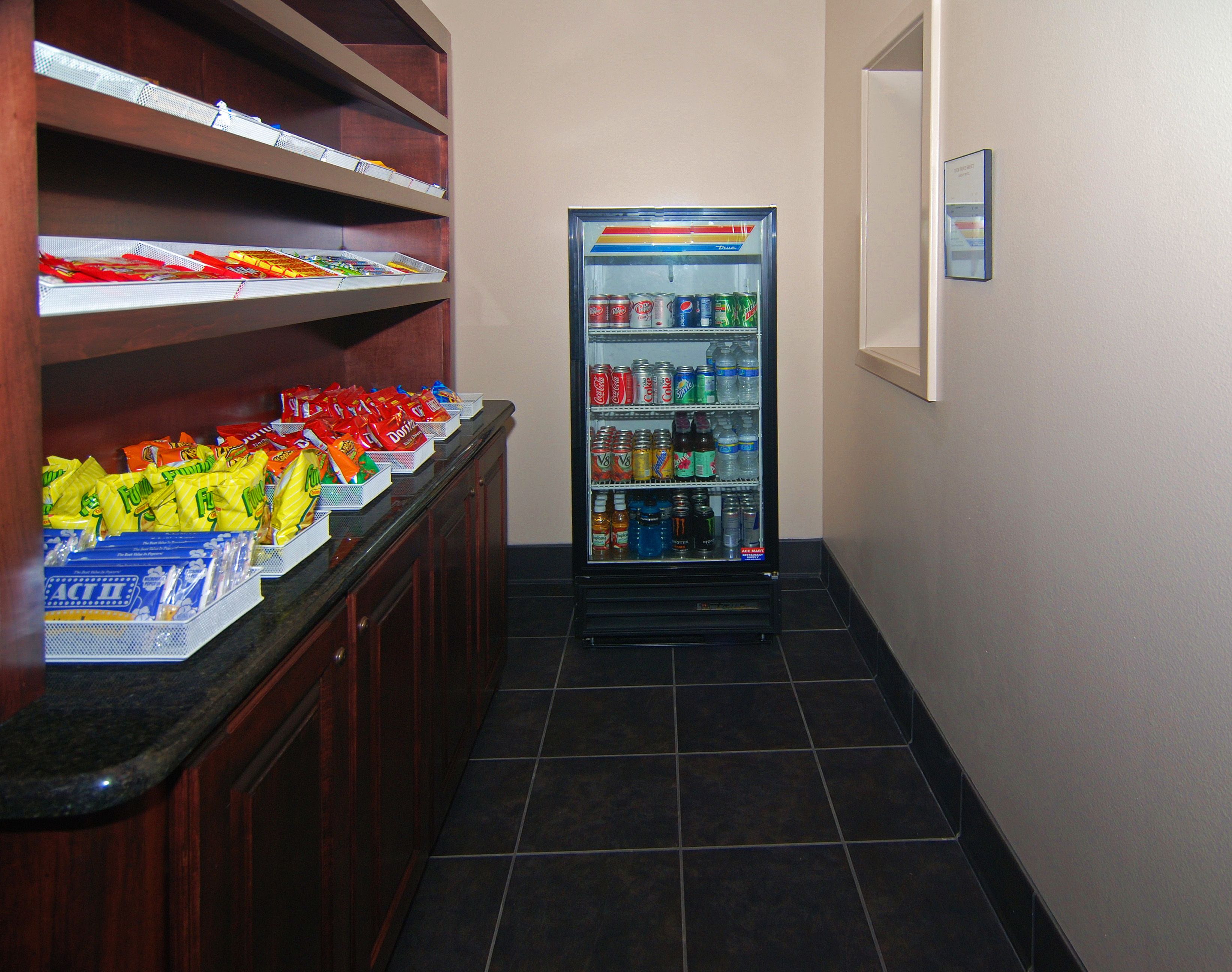 A snack bar with shelves of chips and bags of Doritos, a beverage dispenser with various drinks, and a tiled floor.
