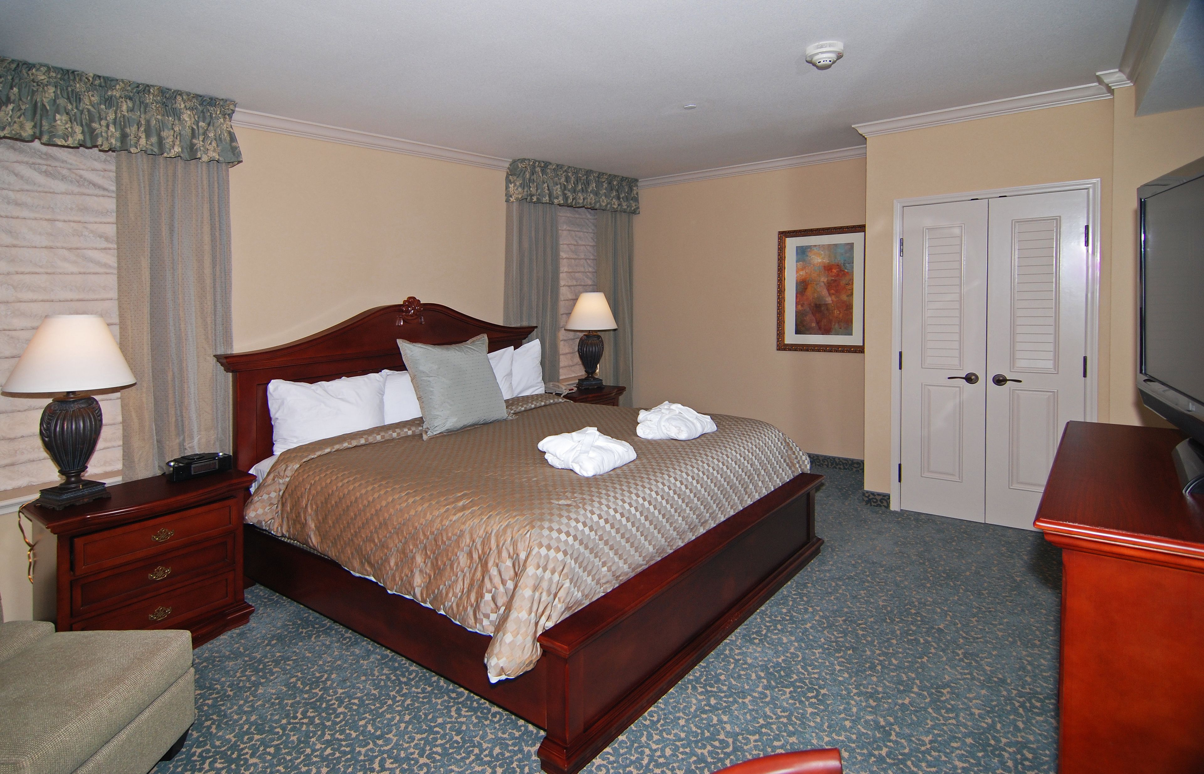 A hotel room with a large bed, two bedside tables with lamps, a chair, a desk, and a television.