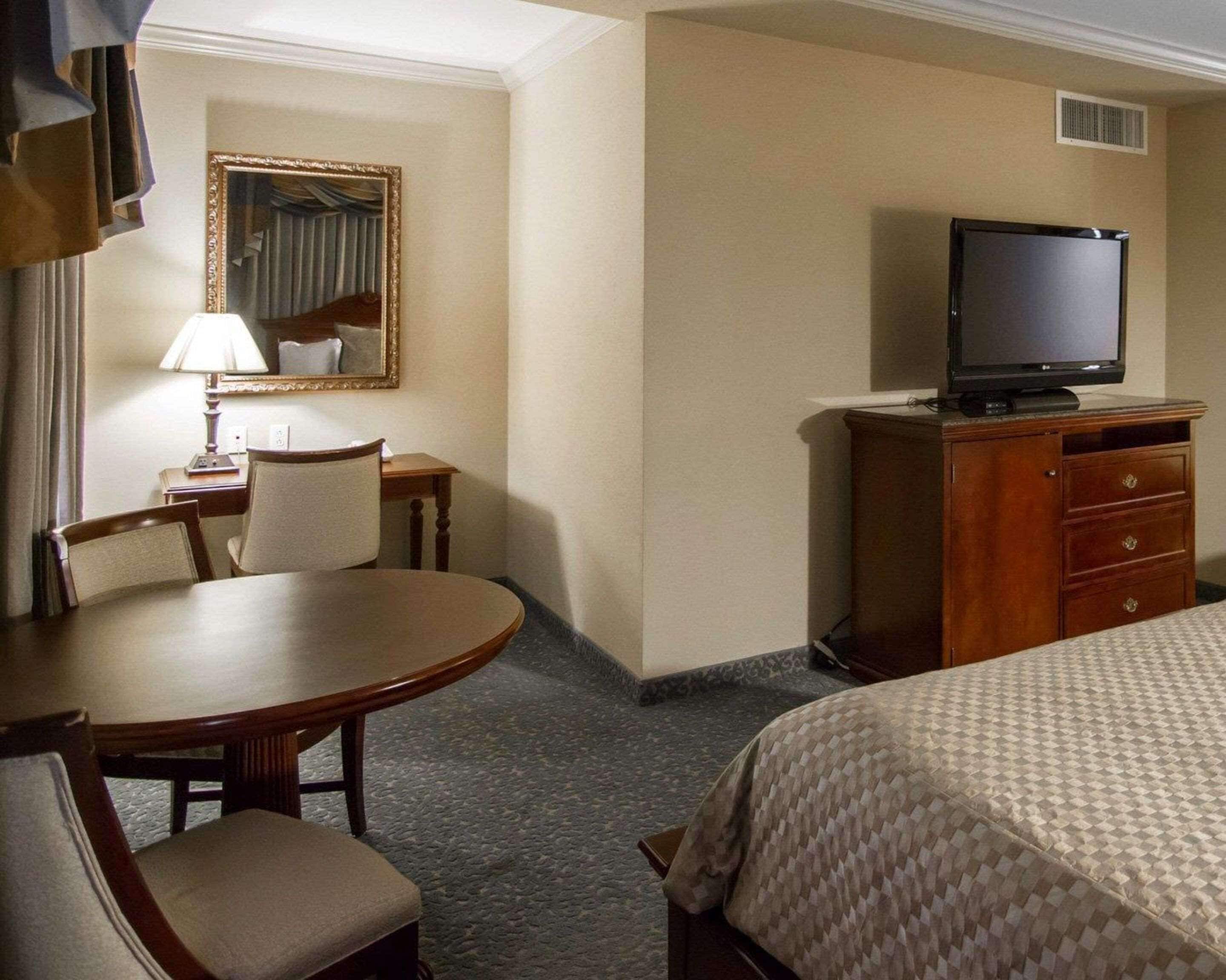 A hotel room with a bed, a desk with a chair, a television on a wooden dresser, and a mirror on the wall.
