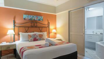 Habitación de hotel con cama, lámparas de noche, un cuadro, baño con espejo y ventilador de techo.