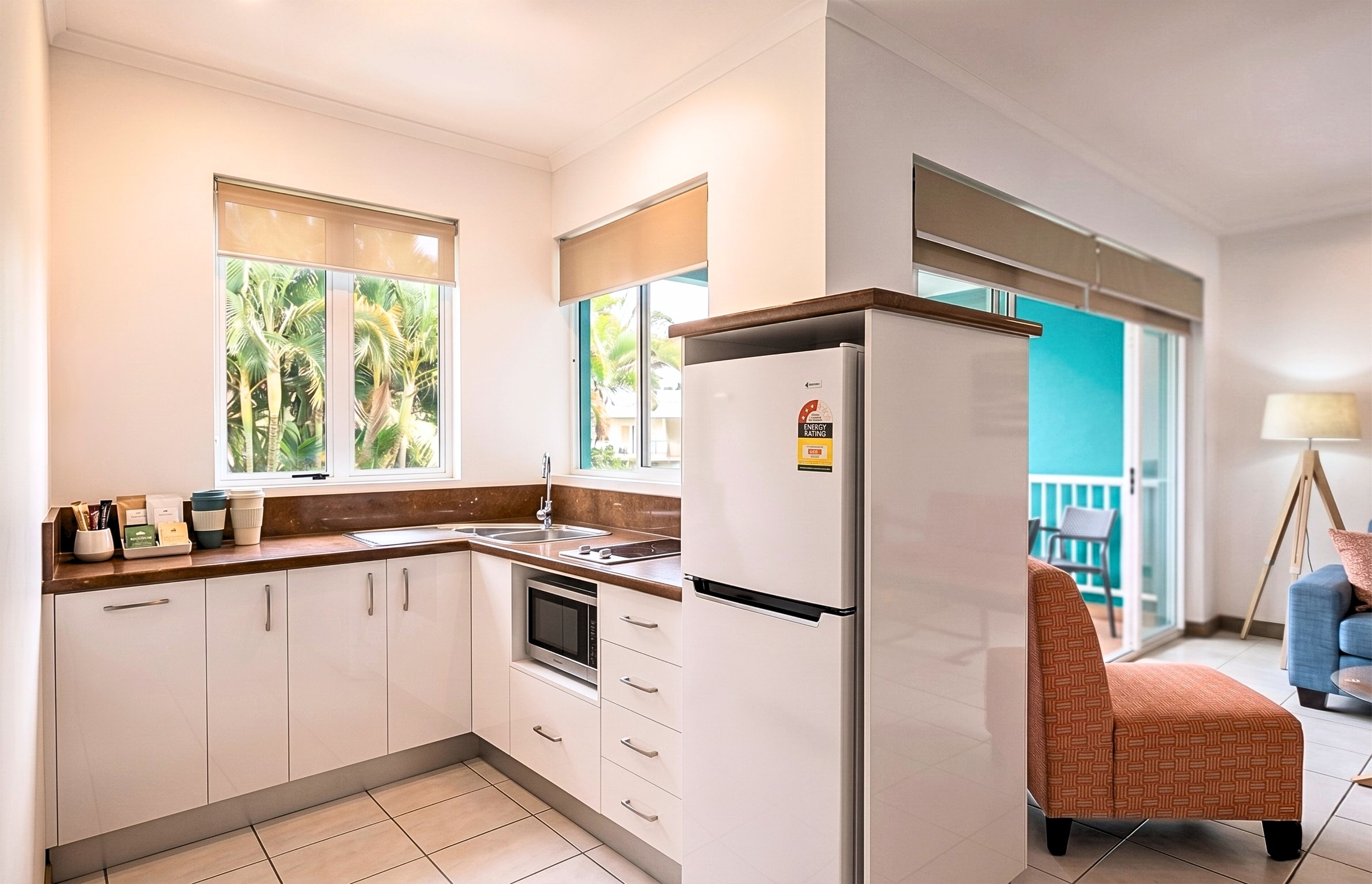 Een moderne keuken met witte kasten, een koelkast en een raam met uitzicht op groen.