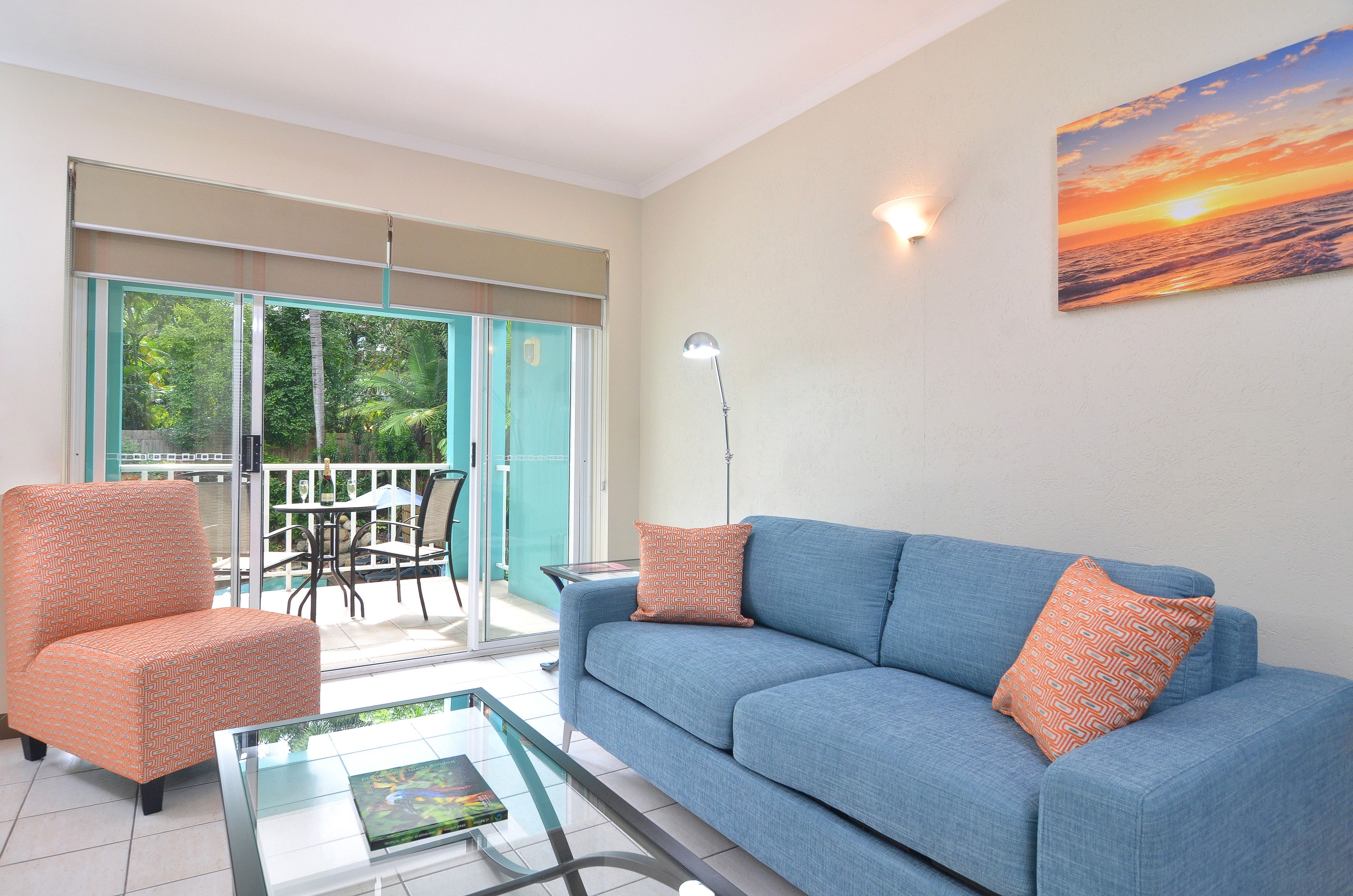 Ein Wohnzimmer mit einem blauen Sofa, einem orangefarbenen Sessel und einem Glastisch.