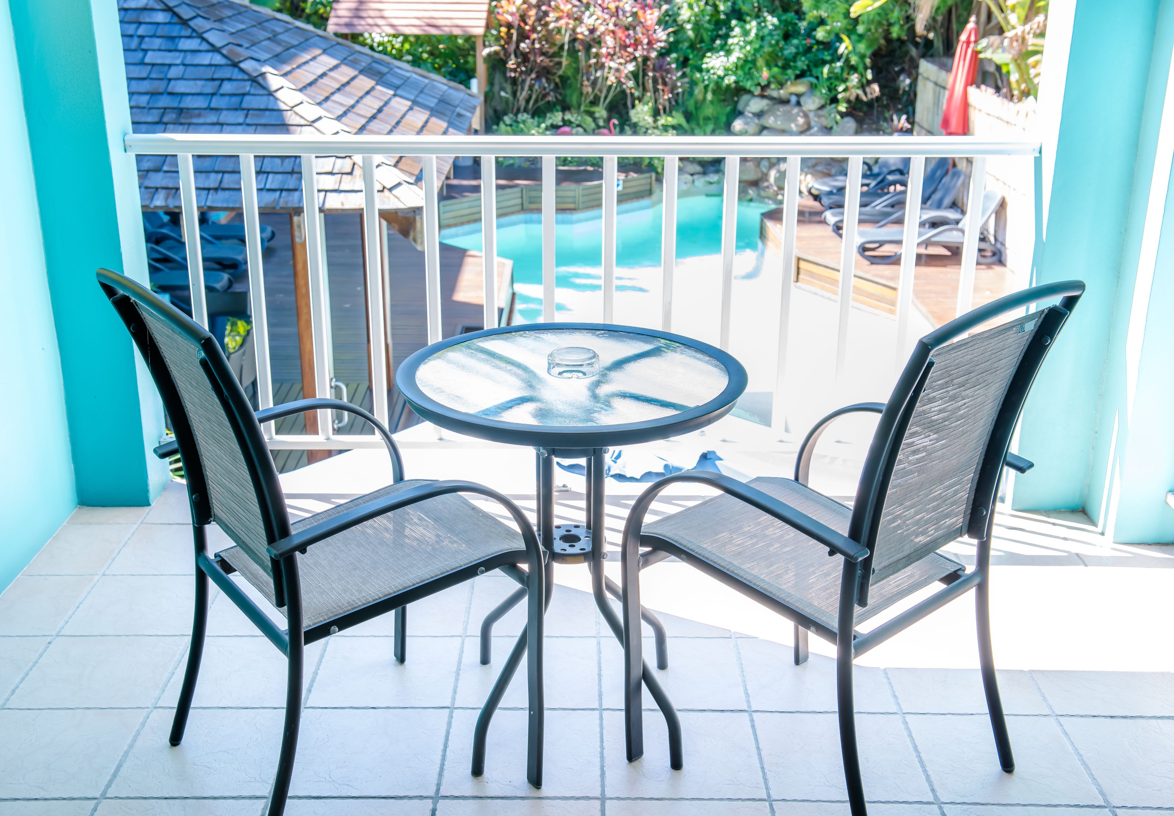 Un balcón con una mesa redonda y dos sillas, con vistas a una piscina y un jardín.