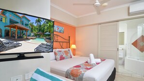 Habitación de hotel con cama, televisor mostrando vista a la piscina, baño con bañera y vistas exteriores a una piscina y un edificio.