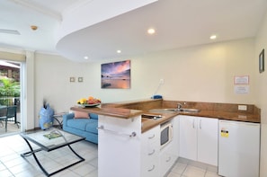 A compact kitchen with a sink, microwave, and a dining area with a glass table and blue sofa. - Le Cher Du Monde (Port Douglas)